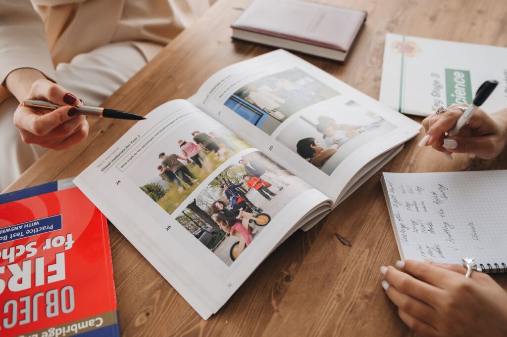 Hands engaged in note-taking and learning from an open book on a wooden table.
